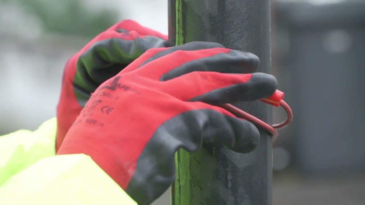 A gloved hand clipping a Genny lead onto a street lighting column